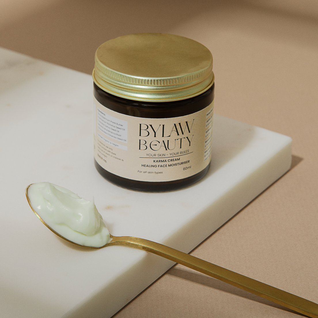 A jar of Bylaw Beauty Karma Cream Healing Face Moisturiser with a spoon beside it, containing a white cream.