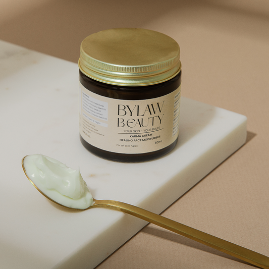 A jar of Bylaw Beauty Karma Cream Healing Face Moisturiser with a spoon beside it, containing a white cream.